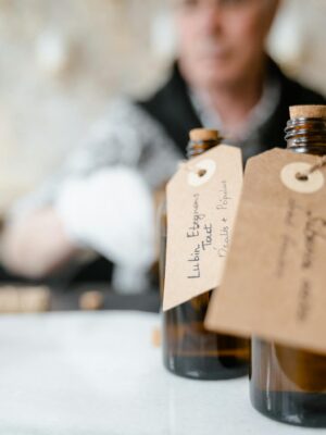 Artisan perfume bottles with handwritten tags on a table, blurred person in background.