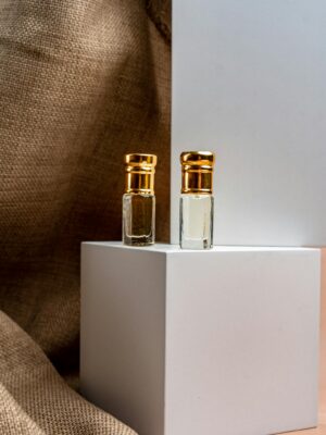 Close-up of two elegant perfume bottles with gold caps on a minimalist white display, evoking luxury.